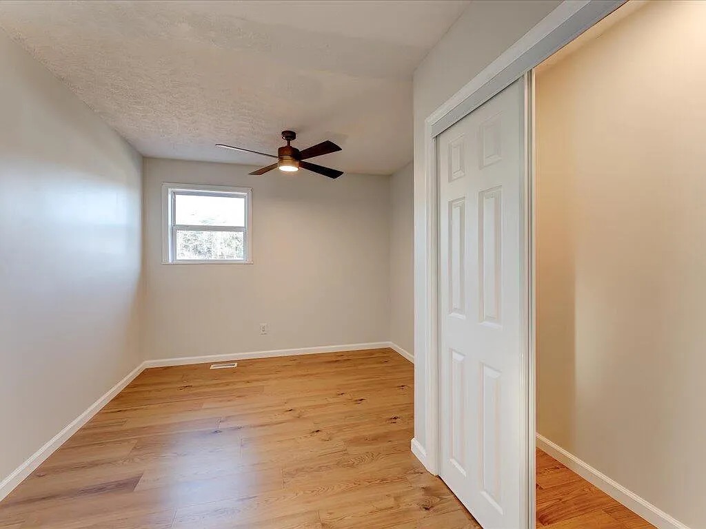 Newly framed bedroom with hardwood flooring, sliding closet doors, and modern ceiling fan