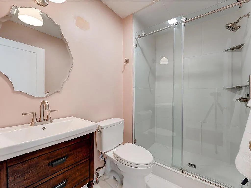Renovated bathroom with frameless glass shower enclosure, wood vanity, and soft blush walls