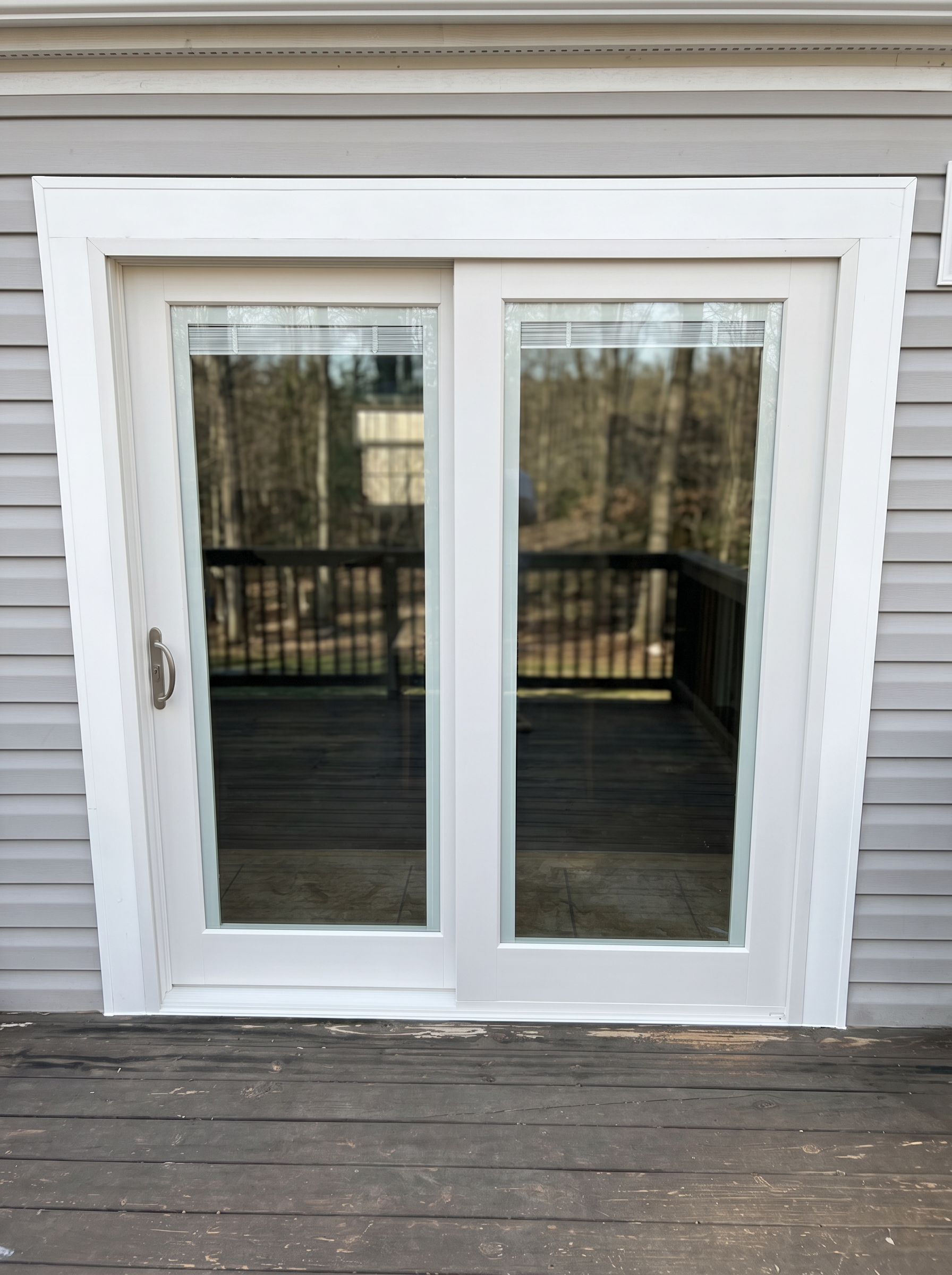Newly installed white vinyl sliding patio door with clean trim on gray siding