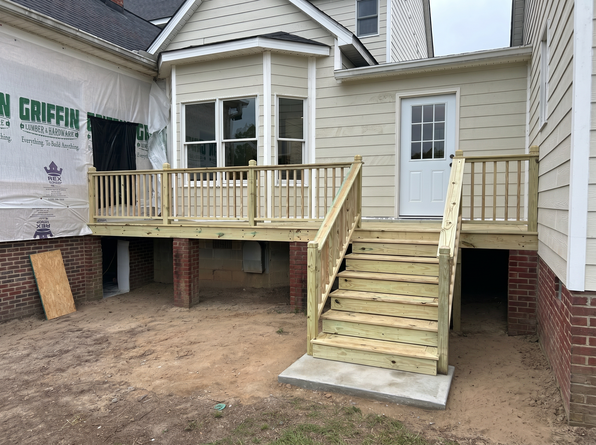 Newly built pressure-treated rear deck with railings, stairs, and concrete landing